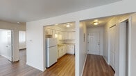 This single-floor residence offers a clean, functional layout with consistent warm wood-look flooring running throughout every room, tying the space together cohesively. The entry hallway provides a welcoming arrival point, flanked by a closet and an electrical panel, leading seamlessly into the main living areas.

The kitchen is a standout feature, outfitted with crisp white cabinetry extending to the ceiling for ample storage, granite-look countertops, and a full suite of white appliances including a gas range, dishwasher, and refrigerator. A dedicated sink area with under-cabinet space completes the well-organized layout.

Adjacent to the kitchen, the living and dining areas offer generous, open space bathed in natural light from large windows dressed with vertical blinds. Baseboard heating runs along the perimeter of the rooms, ensuring year-round comfort.

The bedrooms are bright and airy, each featuring multiple windows that allow natural light to fill the space, along with baseboard heating for added warmth.

The full bathroom is thoughtfully finished with large-format grey tile surrounding the soaking tub and shower, a white vanity with modern hardware, a medicine cabinet mirror, and continued wood-look flooring, creating a clean and contemporary feel throughout.