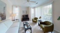 This single-floor residence offers a thoughtfully designed layout with two bedrooms and two full bathrooms. The living room is a standout space, featuring a ceiling fan, plush carpeting, and an abundance of natural light from multiple large windows dressed with vertical blinds and sheer curtains, providing views of surrounding greenery. Crown molding and a smooth transition into the dining area add a refined touch. A bar-height counter separates the kitchen, which is equipped with stainless steel appliances including a refrigerator, microwave, and electric range, complemented by white cabinetry, tile flooring, and a convenient in-unit washer and dryer accessible through a nearby utility closet. Both bedrooms feature soft carpeting and windows that bring in natural light. The primary bedroom is well-proportioned, accommodating a queen bed comfortably alongside storage furniture. Both bathrooms are finished with tile flooring, extended vanities with ample cabinetry, and shower-tub combinations. Overall, the residence maintains a clean, neutral palette throughout, creating a cohesive and comfortable living environment.
