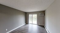 This 670 sq ft, single-floor apartment in Cincinnati, OH features 2 bedrooms, 2 bathrooms, a living room, kitchen, and closet. The living room boasts gray wood-look flooring, neutral walls, a textured ceiling, and a sliding glass door that floods the space with natural light and outdoor views. The galley kitchen includes rich dark cabinetry, granite-look countertops, a stainless steel sink, and black appliances. Both bedrooms feature plush carpet and wall-unit climate control. The primary bedroom measures 150 sq ft with a built-in closet. Bathrooms include a soaking tub and shower.