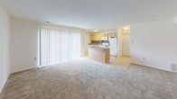 This single-floor residence offers a clean, neutral aesthetic throughout, with white walls and warm beige carpeting that create a bright and inviting atmosphere. The open-concept living area flows seamlessly into the kitchen, anchored by a peninsula with granite countertops that doubles as a breakfast bar. Large vertical blinds along a floor-to-ceiling sliding door bathe the living space in natural light while providing privacy when needed. The kitchen is thoughtfully appointed with light oak cabinetry, granite countertops, a mosaic tile backsplash in gray and brown tones, and white appliances including a gas range, built-in microwave, dishwasher, and refrigerator. Tile flooring in the kitchen provides a practical transition from the carpeted living areas. The bedrooms are generously sized, featuring neutral carpet, white walls, and windows that invite natural light. The bedroom corridor leads to closeted storage, offering ample organizational space. The bathroom features a full tub and shower combination with clean white tile surround, brushed nickel fixtures, and a mosaic tile floor that adds a subtle decorative touch. Overall, the space presents a functional and well-maintained layout suitable for comfortable everyday living.