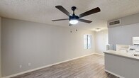 This well-designed one-bedroom, one-bathroom unit is laid out across a single floor, offering a functional and comfortable living experience. The open-concept living room and kitchen area serves as the heart of the home, featuring durable wood-look plank flooring, neutral gray walls, and a textured ceiling fitted with a stylish five-blade ceiling fan with integrated lighting. A window with blinds fills the space with natural light and provides views of the surrounding greenery.

The galley-style kitchen is efficiently arranged with ample white cabinetry on both sides, light stone-look countertops, white appliances including an electric range, microwave, and refrigerator, and a stainless steel sink — all finished with light wood-look flooring for a cohesive aesthetic.

The bedroom offers a comfortable retreat with soft carpeting, neutral walls, a textured ceiling, and a wide three-panel sliding closet that maximizes storage. A ceiling vent ensures effective climate control throughout the room.

The bathroom features a wide vanity with white cabinetry and multiple drawers, a light stone countertop with an integrated sink, a large mirror, and a modern multi-bulb light fixture, creating a bright and clean environment. Wood-look flooring completes the polished look of this thoughtfully designed space.