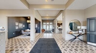 Located at 4100 Lakeview Dr. in Columbus, Ohio, this single-story community clubhouse at Lakeshore Village offers a generously sized, thoughtfully designed gathering space with a cohesive and upscale aesthetic throughout. The signature star-patterned tile flooring unifies the entire layout, providing a distinctive design element that flows seamlessly from room to room.

The main entrance welcomes visitors with a bright, airy foyer featuring transom-topped glass doors, elevated ceilings, and a staffed reception desk illuminated by elegant pendant lighting. Natural light pours in through multiple large windows, creating an open and inviting atmosphere.

Adjacent to the entry, a full-service kitchen is equipped with dark espresso cabinetry, stainless steel appliances, a subway tile backsplash, and a broad island counter with leather bar seating beneath a row of gold pendant lights. A connected dining area features a bold navy wave-pattern accent wall and coordinating artwork.

A private meeting or consultation room offers a dramatic dark-painted interior with a glamorous chandelier, a central round table, upholstered seating, and informational displays mounted on the walls—ideal for presentations or intimate gatherings.

The lounge area provides comfortable seating, a wall-mounted television, ample natural light from clerestory windows, and a billiards table, offering a relaxed, social atmosphere. Double panel doors lead to an additional media or activity room, completing this well-appointed community space.