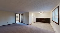 Located at 51 Meadow Brook Rd in Ellington, Connecticut, this single-floor unit offers a practical and functional layout throughout. The living area is generously sized, featuring wall-to-wall carpeting, a textured ceiling, and a sliding glass door with vertical blinds that opens to a private balcony, allowing natural light to fill the space and providing outdoor views. A wall-mounted air conditioning unit and baseboard heating ensure year-round comfort. A half-wall with dark wood paneling visually separates the living and dining areas, adding a warm contrast to the neutral cream walls. The kitchen is efficiently designed with white cabinetry, ample counter space, a double-basin sink, a white electric range, and a full-size refrigerator, all set atop easy-to-clean tile flooring. The bedroom offers carpeted floors, neutral walls, and a closet with dark wood-trimmed doors. An additional carpeted room with a tiled entry serves as a second bedroom or flex space, complete with a window and access to the main entry door. The bathroom features light blue tile wainscoting, a white vanity with mirrored medicine cabinet, a full soaking tub with shower, and tile flooring, creating a clean and classic look throughout.