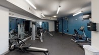 Located at 1399 Walton Way in Augusta, Georgia, this fitness center is a well-equipped, single-floor facility designed to support a comprehensive workout experience. The space is defined by its bold teal accent walls and crisp white ceilings, creating an energetic yet clean atmosphere. Durable rubber flooring covers the entire area, providing safety and comfort for a wide range of exercises.

The cardio zone features Matrix-brand treadmills and elliptical machines positioned near large windows that bring in natural light and offer exterior views, making workouts feel open and less confined. Wall-mounted flat-screen TVs are positioned throughout the space to keep users entertained during exercise sessions.

The strength training area is generously equipped with a cable machine, a weight bench, a Hoist functional trainer, and a dedicated dumbbell and medicine ball rack. Mirrors line one wall, enhancing the sense of space and allowing users to monitor their form. For functional fitness, the facility includes a TRX suspension training system and a freestanding Everlast MMA punching bag station, catering to boxing and bodyweight training enthusiasts.

Overhead fluorescent lighting ensures the entire space is well-lit throughout the day. Fitness club rules are posted prominently, and the layout allows for comfortable movement between stations, making this a practical and versatile fitness facility.
