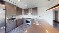 This contemporary two-story residence showcases a refined modern design throughout both levels. Wood-look porcelain tile flooring flows consistently across the space, providing a cohesive aesthetic that complements the clean, neutral palette of the interiors.

The gourmet kitchen is a standout feature, equipped with a professional-grade stainless steel range, a sleek wall-mounted range hood, and built-in double ovens. Rich, wood-grain cabinetry extends floor to ceiling, while a dramatic marble-look backsplash adds visual depth. A generous island with an undermount sink and quartz countertop anchors the space.

The primary bathroom offers a spa-like experience, featuring a freestanding soaking tub, dual undermount sinks set into dark wood vanities with ample drawer storage, illuminated mirrors, and marble-look tile flooring. A secondary bathroom provides a modern vanity with a vessel-style sink and backlit mirror.

Multiple living areas benefit from soaring ceilings and recessed lighting. One level features floor-to-ceiling windows along an entire wall, flooding the space with natural light and offering sweeping city views. A staircase connects the two floors. The residence also includes two well-appointed walk-in closets with custom built-in shelving, hanging rods, and integrated drawer units.