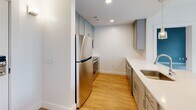 Located at 180 Friendship St in Providence, Rhode Island, this thoughtfully designed residence offers three bedrooms, two bathrooms, and a kitchen within a compact, efficiently arranged single-floor layout. The kitchen is a standout feature, showcasing gray shaker-style cabinetry, a subway tile backsplash, stainless steel appliances including a refrigerator, range, and microwave, light quartz countertops, and warm hardwood-style flooring. A pendant light adds a modern touch above the counter space. The bedrooms are finished with soft carpeting and neutral wall tones, each benefiting from natural light through double-hung windows that frame views of surrounding greenery and neighboring architecture. The primary bedroom includes a closet and direct access to an adjoining bathroom. Both bathrooms are clean and contemporary — one features a glass-enclosed walk-in shower with white tile surround, while the other offers a white vanity with a framed mirror and tile flooring. Throughout the unit, white trim, recessed lighting, and a consistent neutral palette create a bright, cohesive aesthetic. The overall ambiance is modern, functional, and move-in ready.