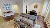 This single-floor residence offers a thoughtfully designed layout that balances comfort and functionality throughout. The open-plan living and dining area serves as the heart of the home, anchored by warm hardwood flooring and crown molding that lend a refined architectural character. Large windows flood the living room with natural light while offering views of the surrounding urban skyline, creating a bright and airy atmosphere. The living area accommodates a generous sectional sofa, a sleek coffee table, and a media console, while a decorative starburst mirror adds a stylish focal point above the dining table, which comfortably seats multiple guests. The galley-style kitchen is efficiently organized with rich dark cabinetry, white countertops, and full appliances, maximizing every inch of the space. Two well-proportioned bedrooms provide restful retreats; the primary bedroom features plush carpeting, crown molding, ample dresser storage, and access to a private en-suite area, while the secondary bedroom offers a similar serene aesthetic with soft carpet and a bright window. The bathroom is finished with clean white tile surrounding a full soaking tub and shower combination. Throughout the residence, a cohesive neutral palette and considered design details create a calm, inviting ambiance.