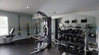 Located at 4912 Signature Dr in Myrtle Beach, SC, this fitness center offers a well-equipped, single-floor workout facility designed to support a comprehensive exercise routine. The space features rubberized flooring throughout, providing both durability and safety during workouts. Floor-to-ceiling mirrors line the walls, enhancing the sense of space and allowing users to monitor their form during exercise. The strength training area is outfitted with a multi-function cable machine capable of a wide variety of resistance exercises, along with a full rack of dumbbells spanning a broad range of weights. A medicine ball rack mounted on the wall adds versatility for functional fitness training. Recessed lighting in the ceiling ensures the space is evenly and adequately illuminated. Cardio equipment is also visible, offering additional options for aerobic training. The overall ambiance is clean, functional, and professionally appointed, reflecting a facility designed with the serious fitness enthusiast in mind. The light-toned walls and mirrored surfaces contribute to an open and energizing atmosphere, making this fitness center a practical and inviting space for residents or members to maintain an active lifestyle.