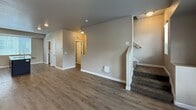 This 1,220-square-foot residence is thoughtfully arranged across three floors, offering 3 bedrooms, 2 full bathrooms, and dedicated laundry. The ground floor (130 sq ft) provides entry access via a staircase connecting to the main living level. The first floor (570 sq ft) serves as the heart of the home, combining the kitchen and living room in an open-concept layout. The kitchen is well-equipped with dark espresso cabinetry, granite-style dark countertops, a gas range, black appliances including a refrigerator and microwave, and a central island with a stainless steel sink. Wood-look plank flooring runs throughout the living areas, and large windows with blinds invite ample natural light. A door off the living area provides outdoor access with views of greenery. The second floor (520 sq ft) houses all three bedrooms, a hallway, and 2 full bathrooms. The primary bedroom measures 160 sq ft, and all bedrooms feature neutral-toned carpet and windows with blinds. Both bathrooms include a full tub/shower surround with chrome fixtures. A dedicated laundry room with full-size washer and dryer hookups and overhead shelving adds everyday convenience. Neutral warm-gray wall tones and white trim carry throughout, creating a cohesive and functional living environment.