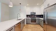 Located at 500 W Camelback Rd in Phoenix, Arizona, this well-appointed 2-bedroom, 3-bathroom residence offers a thoughtfully designed single-floor layout with a clean, contemporary aesthetic. The open-concept kitchen is a standout feature, showcasing two-tone cabinetry with crisp white upper cabinets and soft gray lower cabinets, complemented by a dark tile backsplash and gleaming stainless steel appliances including a gas range, built-in microwave, and French door refrigerator. A peninsula with a white quartz countertop and undermount sink anchors the kitchen, with pendant lighting adding a modern touch. Light wood-tone flooring flows throughout the main living areas, creating a warm and cohesive feel. The living room is bright and open, benefiting from natural light through blinds-fitted windows. Both bedrooms offer a comfortable scale — the primary bedroom features plush carpeting, a ceiling fan, and a window for natural light, while the second bedroom includes light wood flooring and access to natural light via dual windows and a door. Two dedicated closets provide ample storage. The three bathrooms are finished in a clean, minimalist style, each featuring glass-enclosed walk-in showers, wood-look flooring, and chrome fixtures.