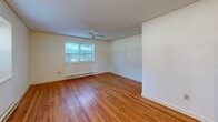Located at 740 Smallwood Dr in Raleigh, NC, this single-floor, one-bedroom, one-bathroom unit offers a practical and well-organized layout. Warm hardwood flooring flows throughout the main living areas and bedroom, lending a classic, inviting character to the space. The combined dining and living room is generously proportioned, bathed in natural light from multiple windows, and equipped with a ceiling fan for year-round comfort. Baseboard heating is present throughout, ensuring consistent warmth. The kitchen is compact yet efficiently designed, featuring white cabinetry, a coil-burner electric range, a full-size refrigerator, and a single-basin sink — all accented by a window that brings in natural light. The bedroom offers a comfortable footprint, with multiple doors providing access to closets, adding notable storage versatility. Three closets total are found throughout the unit, a practical advantage for everyday living. The bathroom includes a vanity with a wood-tone cabinet, a large wall mirror, tiled tub-shower combination, and a window for natural ventilation. Two hallways connect the spaces efficiently. The unit's clean white walls, consistent flooring, and well-distributed natural light throughout create a bright, functional living environment.