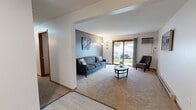 This efficiently designed single-story home makes thoughtful use of its space across three bedrooms, one bathroom, a living room, and a combined kitchen and dining area. The living room serves as the heart of the home, featuring neutral carpet, a calming blue-gray accent wall, and a sliding glass door that floods the space with natural light while offering a pleasant outdoor view. A wall-mounted air conditioning unit provides climate control, and the open layout connects seamlessly to the rest of the home. The galley-style kitchen is fitted with warm oak cabinetry, gray laminate countertops, a stainless steel sink, and black appliances including a range and refrigerator. Light wood-style flooring adds a clean, modern touch. Adjacent to the kitchen, the dining area features the same light flooring and includes a closet for additional storage. The primary bedroom is a comfortable retreat with carpeted floors, a window overlooking greenery, and ample room for furnishings. Additional bedrooms offer flexible use. The shared bathroom is finished with wood-toned cabinetry, a single vanity, and a shower-tub combination. Throughout, warm wood trim and neutral tones create a cohesive and practical living environment.