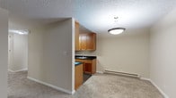 This single-floor space is designed with a practical, straightforward layout that maximizes functionality. The kitchen is a standout feature, outfitted with warm-toned wood cabinetry, dark granite-style countertops, and dark hardwood-style flooring. Black appliances, including a range, refrigerator, and microwave, complement the cabinetry, while ample upper and lower cabinet storage adds convenience. A double basin sink with a window-adjacent position completes the workspace.

Adjacent to the kitchen, the living area is generously sized and finished with neutral carpet throughout, contributing to a comfortable, understated atmosphere. Textured popcorn ceilings and neutral beige walls carry consistently through the space. A sliding glass door in the living area provides direct access to a ground-level patio and frames views of mature trees and landscaping, allowing natural light to filter in. A wall-mounted heating unit ensures year-round comfort.

The bedroom is spacious and similarly carpeted, with a second sliding glass door offering additional outdoor access and natural light. The bathroom is efficiently appointed, featuring a tub and shower combination enclosed by frosted sliding glass doors with chrome hardware, a countertop sink, and a large mirror with overhead lighting.