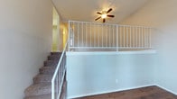 This thoughtfully designed residence offers a comfortable and functional layout spread across multiple levels connected by a carpeted staircase with white metal railings. The main living area features rich hardwood flooring and soaring vaulted ceilings that create an open, airy atmosphere. A wall-mounted HVAC unit and large windows with blinds allow for natural light and climate control throughout the space.

The kitchen is efficiently designed with white cabinetry, speckled granite-style countertops, a stainless steel double sink, a white electric range with overhead ventilation, and a window that brings in natural light — making it both practical and bright.

The bedrooms are finished with wall-to-wall carpeting and textured ceilings, offering a quiet and comfortable retreat. Each room features closet space and windows with blinds. The neutral color palette throughout the bedrooms lends a clean, versatile feel.

The bathrooms are finished with white vanity cabinetry, speckled countertops, framed mirrors, and chrome fixtures. One bathroom includes a full tub-shower combination with a curved surround and hardwood flooring, while the other features stylish vanity lighting above the mirror.

The upper loft level, accessible via the staircase, is open to the living area below and is outfitted with a ceiling fan — adding both functionality and charm to the overall layout of this inviting home.