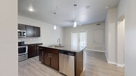Located at 7210 Potranco Road in San Antonio, Texas, this one-bedroom, one-bathroom unit offers a well-designed single-floor layout that maximizes functionality and comfort. The open-concept living and kitchen area forms the heart of the space, featuring light wood-look flooring, neutral walls, and a ceiling fan that enhances airflow. The kitchen is appointed with rich dark espresso cabinetry, granite-style dark countertops, a subway tile backsplash, and a full suite of stainless steel appliances including a range, microwave, dishwasher, and refrigerator. A central island with pendant lighting provides additional prep and dining space. The living area connects directly to a private patio through French doors, inviting natural light throughout. The bedroom is carpeted and generously proportioned, fitted with a ceiling fan and a large window. Four closets, including a walk-in with wire shelving, offer abundant storage. The bathroom includes a dark-vanity with a wide mirror, granite-style countertop, and a soaking tub surrounded by classic white subway tile. A dedicated laundry room houses a full-size washer and dryer. A hallway and utility room round out this thoughtfully planned residence.