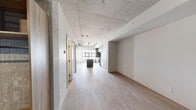 Located in Calgary, AB, this one-bedroom, one-bathroom unit showcases a compelling industrial-modern aesthetic that blends raw architectural elements with contemporary finishes. The open-concept living area is anchored by striking exposed concrete ceilings that lend an urban edge, while light wood-tone flooring runs throughout, creating a warm contrast to the cooler tones above. A sleek sliding barn door separates the living space from the bedroom, adding both function and character.

The kitchen is a standout feature, offering a central island with a dark countertop, grey flat-panel cabinetry, a tiled backsplash, and a full suite of stainless steel appliances including a refrigerator, gas range, dishwasher, and built-in microwave. Large windows flood the kitchen with natural light and frame views of the Calgary cityscape.

The bedroom continues the industrial theme with an exposed concrete accent wall and a generous window offering elevated city views and ample natural light. A dedicated closet area with built-in shelving provides practical storage.

The bathroom is finished with grey square mosaic tile surrounding the soaker tub and shower, large-format floor tiles, a wood-toned vanity with stone-look countertop, and matte black hardware throughout, completing the cohesive modern palette.