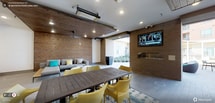 This indoor/outdoor living area is thoughtfully designed to blur the boundary between interior comfort and open-air enjoyment. The space features a striking combination of warm wood-paneled ceilings and exposed brick accent walls, creating a welcoming, lodge-inspired atmosphere. Overhead, ceiling-mounted infrared heaters and recessed lighting ensure year-round usability, while a ceiling fan adds additional climate control.

A large, dark-stained wood dining table surrounded by bold yellow woven chairs serves as the central gathering point, anchored by a patterned area rug. Along one wall, a built-in fireplace adds ambiance and warmth, positioned beneath a wall-mounted flat-screen television—ideal for entertaining. A comfortable upholstered lounge sofa with gray and yellow accent pillows offers a more relaxed seating option nearby.

A wide, retractable opening connects the covered area directly to an exterior courtyard, flooding the space with natural light and providing seamless flow between indoors and outdoors. The overall design balances functionality with a modern, inviting aesthetic suited for both casual gatherings and social events.