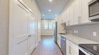 Located at 600 E North Grove Blvd in Waxahachie, TX, this thoughtfully designed 2-bedroom, 1-bathroom residence offers a clean, modern aesthetic throughout its efficiently utilized single-floor layout. The galley-style kitchen is a standout feature, showcasing white shaker cabinetry with brushed nickel hardware, granite-look countertops, a decorative tile backsplash, and a full suite of stainless steel appliances including a refrigerator, dishwasher, microwave, and range. Recessed lighting illuminates the space, while light wood-look flooring flows seamlessly throughout the entire unit, lending a warm, cohesive feel. The two bedrooms are bright and comfortable, with large windows fitted with blinds that invite natural light. The spacious primary bedroom offers generous room for furnishings. The bathroom is well-appointed with large-format gray tile surrounding the soaking tub and shower, a white vanity with stone-look countertops, and ample overhead cabinet storage. A private balcony accessible from the unit features sleek horizontal metal railings and offers open sky views of the surrounding community, providing a pleasant outdoor retreat. The overall ambiance is fresh, contemporary, and move-in ready.