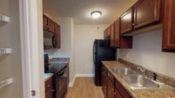 This single-floor apartment at Stone Crest Apartments offers a cohesive and functional layout spread across a well-organized floor plan. The galley-style kitchen is outfitted with rich, dark wood cabinetry, granite-look countertops, a full suite of black appliances—including an electric range, built-in microwave, refrigerator, and dishwasher—and a double stainless steel sink. Light wood-look flooring runs continuously throughout the unit, creating a unified and easy-to-maintain aesthetic.

The spacious living area features neutral beige walls, a ceiling fan, and an open sightline toward the kitchen, fostering a connected, airy feel. A dedicated entry area with a full-size door provides a clear transition into the living space. The bedrooms are well-proportioned, each featuring windows with blinds that allow natural light, flush-mount ceiling fixtures, and the same consistent wood-look flooring.

The bathrooms are clean and functional, each featuring a tub-shower combination with a curtain rod, a toilet, and a wood-vanity with a white countertop and sink, complemented by a large mirror. Hallways connect the private areas of the unit efficiently, maintaining a logical and comfortable flow throughout.