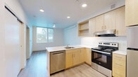 Located at 6823 SW Clinton Street in Tigard, Oregon, this efficient one-bedroom, one-bathroom unit offers a thoughtfully designed single-floor layout with modern finishes throughout. The open-concept living and kitchen area is bright and airy, featuring light hardwood-style flooring, recessed lighting, and a large window that draws in natural light while offering views of the surrounding neighborhood.

The kitchen is well-appointed with light maple cabinetry, white countertops, open shelving, and a full suite of stainless steel appliances including an electric range, dishwasher, and refrigerator. A peninsula with a built-in sink provides additional counter space and separates the kitchen from the living area, creating a functional and social layout.

The bedroom is a clean, minimalist space with light-toned walls, matching hardwood-style flooring, and a tall vertical window that provides natural light and exterior views. Two closets offer practical storage solutions throughout the unit.

The bathroom features a warm maple vanity with a white countertop and undermount sink, a full soaking tub with shower, and a clean, white tile surround. The unit also includes a wall-mounted climate control unit for personalized comfort. Overall, the space presents a clean, contemporary aesthetic well-suited for efficient modern living.