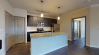 This single-story residence is designed with a contemporary aesthetic, combining functionality and modern finishes throughout its well-organized layout. Dark hardwood-style flooring runs consistently across the living areas, bedrooms, and bathrooms, creating a cohesive visual flow.

The kitchen serves as a central highlight, anchored by a large island with a granite countertop and an integrated sink, illuminated by pendant lighting overhead. Dark espresso cabinetry extends to the ceiling, providing generous storage, while a white subway tile backsplash and a full suite of stainless steel appliances — including a refrigerator, range, and built-in microwave — complete the space. The kitchen opens directly to the living area, which features crown molding and a ceiling-mounted light fixture.

Bedrooms are finished with the same wood-style flooring and neutral walls, with at least one room offering dual windows that allow natural light and exterior views. Walk-in closet access is visible from one of the bedroom areas.

The bathrooms are appointed with dark vanity cabinetry, granite countertops, large framed mirrors, and tiled tub-shower combinations, maintaining the consistent design language found throughout the residence.