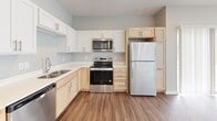 This efficiently designed 1-bedroom, 1-bathroom single-floor unit offers a thoughtfully laid-out living space across a compact yet functional footprint. The open-concept kitchen flows seamlessly into the dining and living areas, creating a cohesive and practical layout. The kitchen is well-appointed with a full suite of stainless steel appliances, including a refrigerator, electric range, built-in microwave, and dishwasher. Cabinetry features a two-tone design with white upper cabinets and light natural wood lower cabinets, complemented by clean white countertops and a stainless steel sink. Durable wood-look flooring runs throughout the main living areas, adding warmth and visual continuity. The living and dining area is bright and airy, benefiting from multiple windows fitted with horizontal blinds and a sliding glass door that opens to an outdoor patio, inviting natural light throughout the day. The bedroom is a comfortable, private retreat with its own window, a ceiling fan, and the same wood-look flooring. A dedicated closet provides convenient storage. The bathroom includes a walk-in shower with a clean, all-white surround. Neutral gray walls and a textured ceiling complete the modern, move-in-ready aesthetic of this practical and inviting space.