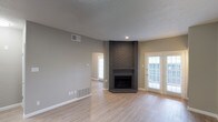 This single-floor Dallas property offers a well-designed layout with a clean, neutral aesthetic that creates a welcoming and functional living environment. The main living area is a standout, anchored by a charming corner brick fireplace that serves as a natural focal point. Light wood-style flooring runs throughout, complementing the soft gray and beige wall tones and lending the space a bright, airy feel. A textured ceiling adds subtle visual depth to the room. French doors with slatted blinds provide an elegant connection to the outdoors, inviting abundant natural light while maintaining privacy. Recessed lighting adds warm, directed illumination. Visible HVAC vents integrated into the walls and floors speak to the practical infrastructure of the home. An open passageway leads to an adjacent room, also filled with natural light from a large window, suggesting a seamless, open flow between living spaces. The overall ambiance is modern yet understated, offering a versatile canvas well-suited for a variety of interior styles. The combination of natural light, classic brick detailing, and cohesive finishes makes this Dallas property an inviting and functional place to call home.
