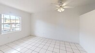 Located in Miami, FL, this efficient one-bedroom, one-bathroom unit offers a well-organized single-floor layout that makes smart use of its space. Throughout the unit, bright white ceramic tile flooring creates a clean, cohesive look that reflects natural light and lends a cool, airy feel suited to the South Florida climate.

The unit features two distinct living areas, each finished with the same consistent tile work and crisp white walls. One living area is equipped with a ceiling fan with integrated lighting, while the other receives natural light through a large window offering views of the surrounding exterior. These spaces are open and versatile, easily adaptable to a variety of furniture arrangements.

The kitchen is a compact galley-style space featuring white cabinetry, speckled laminate countertops with a stainless steel sink, a matching decorative backsplash, and a full-size refrigerator with in-unit range.

The bedroom is a well-proportioned room with its own ceiling-mounted light fixture, a window for natural light and ventilation, and direct access to both a closet and the bathroom, enhancing functionality and privacy.

The bathroom is a standout feature, showcasing a full tub-shower combination surrounded by classic white mosaic tile accented with colorful red, blue, and yellow square inlays — a charming retro detail. A window above the tub provides natural light and ventilation, completing this thoughtfully designed space.