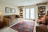 This single-story residence in Tuscaloosa, Alabama offers a well-organized layout with multiple bedrooms, two bathrooms, a galley-style kitchen, and a comfortable living area. Throughout the home, neutral beige tones and textured ceilings create a warm, cohesive atmosphere, while ceiling fans in each bedroom promote year-round comfort.

The bedrooms are carpeted and generously sized, each featuring a ceiling fan and windows dressed with sheer curtains that allow natural light to filter through softly. The primary bathroom is notably spacious, with white tile flooring, a wide vanity with oak cabinetry, a large mirror, and a separate water closet with a window. A built-in linen closet adds practical storage. The secondary bathroom features a similar oak vanity, a wall-mounted light bar, and a tub-shower combination.

The galley kitchen is lined with warm oak cabinetry on both sides, offering generous counter and storage space, a double sink, and white appliances including a range, microwave, refrigerator, and dishwasher. Light tile flooring runs underfoot.

The living area is a standout feature, showcasing a built-in bookshelf alcove and French doors that open to the outside, inviting natural light and outdoor views into the space. Plush carpet and a classic layout complete the inviting interior.