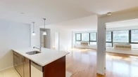 Located at 26-38 21st Street in Astoria, Queens, this 3-bedroom, 1-bathroom residence offers a well-designed layout across a single floor. The open-concept living and kitchen area serves as the heart of the home, where warm hardwood flooring extends throughout and large windows flood the space with natural light while offering views of the surrounding neighborhood. The kitchen is outfitted with rich dark wood cabinetry, stainless steel appliances including a refrigerator, gas range, and microwave, a tiled backsplash, and a generous peninsula with a white quartz countertop and an undermount sink, illuminated by pendant lighting overhead. The spacious living area provides ample room for entertaining or relaxing. Each of the three bedrooms features the same warm hardwood floors and large windows with built-in HVAC units, ensuring comfort year-round; the primary bedroom includes a double-door closet for added storage. The bathroom is finished with dark tile flooring, a wood vanity with a white countertop, a mirrored medicine cabinet, and a full tub and shower with neutral tile surround. Clean white walls and a consistent modern aesthetic give the entire residence a bright, cohesive feel.