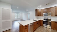 Located at 92 Plains Rd in Milford, Connecticut, this single-floor residence offers a clean, modern design with an open and functional layout. The heart of the home is an open-concept kitchen and living area, where warm-toned wood cabinetry pairs with crisp white quartz countertops and a peninsula island that flows seamlessly into the living space. A full suite of stainless steel appliances — including a refrigerator, range, microwave, and dishwasher — equips the kitchen for everyday use. Recessed lighting throughout keeps the interior bright and inviting, while large windows in the living area allow natural light to fill the space. Hardwood-style flooring runs throughout, lending a cohesive and polished aesthetic to every room. The bedroom features a sliding-door closet as well as access to a generously sized walk-in closet outfitted with wire shelving on multiple walls, providing abundant storage. The bathroom is finished with a combination tub and shower enclosed by sliding glass doors with chrome hardware, set against neutral tile flooring and clean white walls. Additional utility access panels are visible in the common areas, reflecting thoughtful, practical design. Overall, this residence delivers a fresh, move-in-ready living environment with modern finishes throughout.