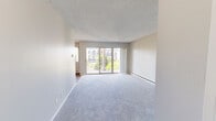 Located at 10500 Meridian Ave N in Seattle, WA, this well-laid-out 2-bedroom, 2-bathroom unit offers a comfortable and functional living environment across a single floor. The open living room is bathed in natural light from large sliding glass doors that lead to a private balcony, offering pleasant views of surrounding greenery and the neighboring building. Plush carpeting runs throughout the living areas and bedrooms, adding warmth underfoot, while wood-style flooring flows through the kitchen and bathrooms. The galley-style kitchen is efficiently designed with ample white cabinetry on both sides, stone-toned countertops, a double sink, and white appliances including an electric range and refrigerator. The spacious primary bedroom features mirrored sliding closet doors and a window that invites natural light. The second bedroom includes a built-in closet with shelving and a large window with outdoor views. Both bathrooms are clean and functional — one features a full tub and shower combo with white surround and wood-style flooring, while the other offers a vanity with a stone-toned countertop. Each room is equipped with baseboard heating. The overall ambiance is bright, neutral, and move-in ready.