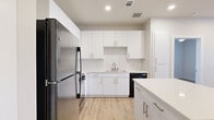 This single-floor unit offers a well-designed layout across two bedrooms, two bathrooms, and a combined kitchen and living area, all connected by two hallways and a dedicated closet. The interior maintains a clean, modern aesthetic throughout, anchored by light wood-tone flooring that runs continuously across all rooms.

The kitchen serves as a central highlight, featuring crisp white cabinetry extending to the ceiling, white countertops, and a suite of black appliances including a refrigerator, range, microwave, and dishwasher. A white kitchen island provides additional workspace and adds definition between the kitchen and living area. Recessed lighting illuminates the space efficiently.

The primary bedroom is a comfortable size and benefits from natural light through windows fitted with white blinds. The second bedroom similarly features wood flooring, neutral walls, and window access to natural light. Both rooms offer a clean, versatile canvas.

The two bathrooms share a consistent design language: white vanities with undermount sinks, white countertops, full tub-shower combinations with tiled surrounds, and light tile flooring. Brushed nickel fixtures and large mirrors complete each bathroom's functional layout.

Overall, the unit presents a cohesive, contemporary aesthetic with neutral tones throughout.