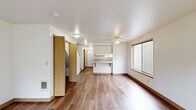 Located at 1813 Drexler Ln NE in Keizer, Oregon, this two-bedroom, one-bathroom home is thoughtfully arranged across two floors. The main level features an open-concept layout connecting the living area, dining space, and kitchen. Warm wood-look flooring flows throughout, complementing the clean white walls and wood-trimmed accents. A ceiling fan with light fixture serves the living room, which benefits from a large window that brings in natural light and exterior views. The kitchen is well-equipped with white cabinetry featuring wood trim, light-toned countertops, a double sink, dishwasher, and electric range. A peninsula with overhang seating connects the kitchen to the dining area, creating a practical and social layout. A staircase leads to the upper level, where both bedrooms are located. The spacious primary bedroom includes a ceiling fan, a broad window overlooking greenery, and ample room for furnishings. The second bedroom is bright and well-proportioned, also featuring wood-look flooring. A separate bedroom features a built-in closet with sliding wood doors and a clothing rod. Clean, neutral finishes and consistent flooring throughout both floors give the home a cohesive and move-in-ready appearance.