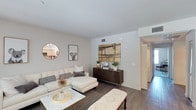 Located at 300-328 S Escondido Blvd in Escondido, California, Unit #211 is a well-appointed single-floor residence designed with comfort and modern aesthetics in mind. The living area serves as the centerpiece of the home, featuring rich hardwood-style flooring that extends throughout the space, creating a warm and cohesive look. Neutral-toned walls provide a clean backdrop that complements a variety of décor styles, while the open layout allows for a natural and easy flow between living and dining areas. Recessed ventilation and ceiling fixtures are neatly integrated into the design, contributing to an uncluttered, polished feel. A hallway leads to the additional areas of the unit, hinting at a well-organized floor plan. The kitchen, visible in the background, features light cabinetry and modern appliances, seamlessly connecting to the main living space. Louvered closet doors in the hallway add a classic architectural detail while maximizing storage functionality. The overall ambiance of the unit is bright, clean, and inviting, making it an ideal space for both relaxing and entertaining. The thoughtful use of space throughout the unit ensures that every area feels purposeful and well-utilized.