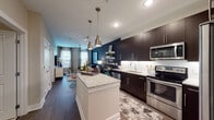 This single-floor residence showcases a contemporary design with a cohesive blend of dark and light tones throughout. The open-concept kitchen is a standout feature, equipped with rich dark espresso cabinetry, granite countertops, a geometric white tile backsplash, and a full suite of stainless steel appliances. A central island provides additional prep space and serves as a natural dividing point between the kitchen and the adjoining living area. Under-cabinet lighting enhances the kitchen's sleek aesthetic.

The living room is anchored by large windows that invite abundant natural light, paired with a bold dark accent wall that adds depth and contrast to the space. The room flows seamlessly from the kitchen, creating an inviting, open atmosphere well-suited for both relaxing and entertaining.

The bedroom continues the bold design language with a dramatic dark accent wall, plush carpeting, and windows dressed in sheer curtains that allow soft, diffused light to fill the room.

The bathroom features a soaking tub with a tiled surround, wood-look tile flooring, and a granite-topped vanity with dark cabinetry consistent with the rest of the home. Recessed lighting provides a clean, modern finish. Overall, the space presents a polished, upscale aesthetic throughout.