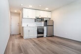 Located at 4765 Hayes Rd in Madison, Wisconsin, this efficiently designed single-floor studio unit offers a clean, modern aesthetic with a thoughtful layout. Light wood plank flooring extends throughout the space, creating a warm and cohesive feel that enhances the sense of openness.

The entrance leads into the main living area, where a built-in kitchenette lines one wall. The kitchen features white shaker-style cabinetry with ample upper storage, a stainless steel refrigerator, a range with oven, an over-the-range microwave, and a compact sink — providing all the essentials in a streamlined configuration. Recessed lighting illuminates the kitchen and living zone, complementing the natural light that enters through a window fitted with blinds.

The living area is open and versatile, offering a blank canvas with neutral walls and consistent flooring. A wall-mounted HVAC unit ensures climate control year-round. Near the entrance, a dedicated closet with a hanging rod and shelving provides practical storage.

The unit includes two bathrooms, each finished with light-toned flooring, white vanities, and clean, minimal fixtures — offering added convenience and privacy. The overall ambiance is bright, functional, and move-in ready, making this a well-appointed space for efficient urban living in Madison.