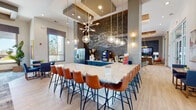 Located at 701 Little Palm Circle in Cape Coral, Florida, this single-story community clubhouse delivers a polished, resort-inspired atmosphere through thoughtful architectural design and upscale finishes. The reception area greets visitors with a striking marble-faced desk, sputnik-style chandelier suspended from a wood-accented tray ceiling, and light wood-look tile flooring that flows throughout the space. Built-in shelving with curated décor and floor-to-ceiling glass doors frame views of the outdoor surroundings, filling the entry with natural light. The Avenue Coffeehouse area features a dramatic exposed brick accent wall with hand-lettered signage, teal cabinetry, stainless steel appliances, and a generous marble-topped island with leather bar seating beneath globe pendant lighting. An adjacent lounge offers comfortable seating and panoramic windows overlooking palm-lined grounds. The games lounge is anchored by a full-size billiards table and shuffleboard, complemented by a wall-mounted fireplace, flat-screen television, and warm amber seating beneath a wood-paneled tray ceiling. A dedicated business center nook provides workstations with ample natural light, completing this well-appointed community facility.