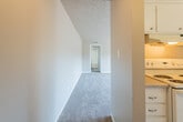 This single-floor residence offers a practical and comfortable layout designed for everyday living. The galley-style kitchen is efficiently arranged with white cabinetry providing ample storage, light countertops, a double-basin sink, a coil-burner electric range, and a full-size refrigerator. Tile flooring runs throughout the kitchen, while a ceiling fan overhead adds airflow and light. The kitchen opens toward the main living area, which is generously proportioned and finished with plush carpet and a textured ceiling. A ceiling fan anchors the living space, and a window with vertical blinds allows natural light to filter in. The entryway features a dedicated overhead light and a solid entry door. A hallway connects the living spaces to the private areas of the residence, where carpeted bedrooms offer comfortable retreats. One bedroom features a window with an outdoor view, while another includes mirrored sliding closet doors and a built-in vanity with a lighted mirror and storage drawers — a thoughtful touch for daily use. The bathroom includes a wide vanity with a single sink, a large mirror with overhead lighting, and an adjacent wet room with a tiled tub-and-shower combination and toilet. Throughout the space, neutral tones and consistent finishes create a cohesive and move-in-ready environment.