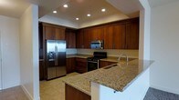 This single-floor space showcases a thoughtfully designed kitchen as its centerpiece. The kitchen is outfitted with rich, dark wood cabinetry that extends to the ceiling, providing generous storage throughout. Granite countertops in warm, earthy tones run along the perimeter and continue onto a central island, which also features a built-in sink — making it both a functional prep area and a natural gathering point.

Stainless steel appliances, including a French door refrigerator with an ice and water dispenser, a gas range, and an over-the-range microwave, complement the cabinetry and contribute to a cohesive, modern aesthetic. Light-toned tile flooring grounds the space and pairs well with the warmer cabinetry tones above.

Recessed lighting is installed throughout the ceiling, providing even, practical illumination across the workspace. The layout follows a functional L-shape with the island anchoring the open side, allowing for efficient movement and workflow. The overall design balances practicality with an upscale finish, making the kitchen a well-equipped and visually appealing core of the space.