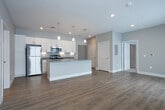 Located at 1700 Harmony Lake Dr in Muskegon, Michigan, this single-floor unit offers a clean, modern design with a neutral color palette and quality finishes throughout. The open-concept kitchen serves as the centerpiece of the living area, showcasing crisp white shaker-style cabinetry extending to the ceiling, sleek gray quartz countertops, and a suite of stainless steel appliances including a gas range, microwave, and refrigerator. A spacious center island with an integrated double sink and elegant pendant lighting above makes the kitchen both functional and visually striking. Light wood-look flooring runs through the main living and kitchen areas, adding warmth to the contemporary aesthetic. The bedrooms are generously sized, finished with soft neutral carpet and fitted with window blinds that allow for natural light. One bedroom features a dedicated walk-in closet with built-in shelving, offering excellent storage capacity. The primary bathroom is well-appointed with an extended white vanity, dual sinks, a large mirror with vanity lighting, and wood-look flooring. A secondary bathroom provides a full tub-shower combination with brushed gold fixtures. The overall layout is thoughtfully designed to maximize functionality while maintaining a bright, cohesive aesthetic throughout.