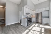 Located at 50 Portland Street in Toronto's vibrant King West neighbourhood, this efficiently designed one-bedroom, one-bathroom unit offers a clean, modern aesthetic throughout. The open-concept main area is anchored by a stunning kitchen featuring high-gloss white cabinetry, a striking marble-effect backsplash, stainless steel appliances including a range, dishwasher, and French door refrigerator, and a stacked washer and dryer unit — all set beneath soaring ceilings that lend a sense of spaciousness well beyond the unit's compact footprint. Light washes in through large windows, casting natural patterns across the pale hardwood-style flooring that runs seamlessly through the main living space and into the hallway. The bedroom is a calm, neutral retreat with its own natural light source through a street-facing window, offering a tranquil urban outlook. The bathroom is finished with floor-to-ceiling marble-effect tile surrounding the soaker tub, complemented by a white vanity and bright, clean fixtures. A connecting hallway with soft carpet underfoot ties the private spaces together. The overall palette of warm whites and light neutrals creates a fresh, contemporary ambiance throughout.
