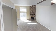 This two-story residence offers a welcoming and functional layout designed with comfort in mind. The main living area serves as the focal point of the home, showcasing a dramatic floor-to-ceiling brick fireplace positioned in the corner — a standout architectural element that adds texture, warmth, and visual interest to the room. The fireplace features a simple wood mantel and a raised brick hearth, lending a classic, cozy character to the space.

Plush wall-to-wall carpeting in a neutral beige tone runs throughout the living area, contributing to a warm and comfortable atmosphere. A large sliding glass door floods the room with an abundance of natural light, creating a bright and airy feel. The textured ceiling adds subtle dimension overhead, while clean white walls and neutral tones throughout provide a versatile backdrop suitable for a variety of interior styles.

A staircase is visible from the living area, connecting the two levels of the home and reinforcing the multi-story layout. A ceiling fan is partially visible, offering practical climate control. Overall, the space presents a clean, open, and light-filled environment anchored by its distinctive brick fireplace centerpiece.