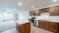 Located at 1625 24th Ave NW in Owatonna, MN, this single-floor, 3-bedroom, 2-bathroom unit offers a well-designed layout with a practical mix of finishes and features throughout. The open-concept kitchen and living area serves as the heart of the home, with the kitchen showcasing rich, warm-toned cabinetry, light granite-style countertops, a central island for additional prep space, and a full suite of stainless steel appliances including a range, microwave, dishwasher, and refrigerator. Light wood-look flooring runs through the kitchen and main areas, lending a clean, cohesive look. The living room is carpeted and benefits from a ceiling fan and access to natural light through a window overlooking the exterior. The three bedrooms are each carpeted and feature neutral white walls with warm wood-trimmed doors and closet access, creating a calm and functional retreat. The primary bedroom is a comfortable size with natural light filtering through a window with blinds. Both bathrooms are clean and functional, with one featuring a full tub-shower combination and another offering a single-sink vanity with warm wood cabinetry, a large mirror, and light wood trim detailing throughout. Overall, the unit presents a tidy, move-in-ready interior with consistent finishes and a well-organized floor plan.