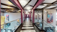 The Ivy's amenity level makes a bold first impression with a sweeping corridor defined by bold magenta columns, coffered ceilings with crystal chandeliers, and a striking black-and-white marble-patterned floor. Glass railings line the mezzanine overlook, offering views of a dramatic double-height entry below adorned with a cascading gold chandelier and vibrant commissioned artwork throughout.

The curved lounge is a standout feature, wrapped in floor-to-ceiling windows that frame expansive outdoor views. Geometric-patterned wallcovering, a tiered crystal chandelier, and a curated mix of velvet seating and contemporary furnishings give the space a refined yet welcoming character.

The fitness facilities are comprehensive and well-appointed. A strength training room with rubber flooring, weight racks, and cable machines is complemented by a dedicated cardio suite featuring a full row of ellipticals and stationary bikes. A separate spin and studio room provides space for group fitness, stocked with cycling bikes and stability equipment.

Rounding out the amenities is a golf simulator lounge, complete with a putting green, a sleek bar counter with bar seating, wood-paneled walls, and pendant lighting — an ideal setting for both recreation and entertaining. Throughout, coffered ceilings and consistent design details unify the entire floor with a polished, upscale aesthetic.