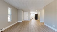 This single-floor unit offers a clean, functional layout designed for comfortable everyday living. The open-concept living area is finished with light-toned laminate flooring and neutral warm-gray walls, creating a bright and welcoming atmosphere. A textured ceiling runs throughout the main living spaces, adding a classic touch. The living room features sliding glass door access to an outdoor balcony area, complemented by a wall-mounted air conditioning unit and baseboard heating for year-round climate control.

The kitchen is a standout feature, showcasing crisp white cabinetry with brushed nickel hardware, marble-look quartz countertops, a gray subway tile backsplash, and a full suite of stainless steel appliances including a dishwasher, stove, and refrigerator. A window above the sink brings in natural light, enhancing the kitchen's bright and modern aesthetic.

The two bedrooms are carpeted for warmth and comfort, each with natural light from windows fitted with horizontal blinds and baseboard heating. The primary bedroom also includes a ceiling fan with integrated lighting. The bathroom features a full soaking tub surrounded by classic white subway tile, offering a clean and timeless finish throughout.