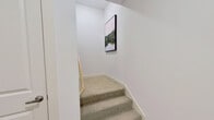 This thoughtfully designed multi-floor residence spans three levels, offering a clean, contemporary aesthetic throughout. The bright, open kitchen is a standout feature, showcasing white shaker cabinetry, a large center island with bar seating, stainless steel appliances, a tiled backsplash, and pendant lighting — all set above warm hardwood-style flooring. A dining area nearby is accented by a bold, large-format painting that adds a vibrant artistic touch to the space.

The living area welcomes natural light through generous windows and a glazed entry door with transom, creating an airy, inviting atmosphere. Bedrooms are well-proportioned and comfortable, with hardwood-style floors, large windows offering neighborhood views, and ample room for relaxing. A walk-in closet with built-in shelving, hanging rods, and organizational storage adds practical functionality to the primary suite.

The bathroom is finished with crisp white cabinetry, a long vanity with an undermount sink, a wide mirror, and wood-look tile flooring, maintaining the home's clean, modern palette. A dedicated laundry room houses a full-size washer and dryer alongside built-in shelving for added convenience. Carpeted stairs connect the floors, each adorned with framed artwork, reinforcing a curated, welcoming atmosphere throughout this well-appointed residence.