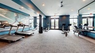 Located at 4322 White Birch Avenue in Smyrna, Tennessee, this fitness center offers a thoughtfully designed workout environment across a single open floor. The space is defined by bold teal accent walls contrasted against crisp white ceilings, creating an energetic and motivating atmosphere. Plush carpet tile flooring covers the entire area, providing comfort underfoot during workouts.

The facility is well-lit through a combination of recessed ceiling lights and large glass double doors that invite natural light while offering views of the surrounding outdoor environment. Ceiling fans provide additional air circulation throughout the space.

The fitness center is comprehensively equipped across multiple workout zones. A dedicated cardio area houses treadmills, elliptical machines, and cycling bikes with digital displays. A free weights section features a full rack of dumbbells arranged on tiered shelving, accompanied by a flat bench. Additional workout accessories, including medicine balls and resistance equipment, are mounted along the walls for easy access.

Full-length mirrors are strategically positioned throughout the room, enhancing the sense of spaciousness and allowing users to monitor their form. A motivational mural adorning one wall adds a dynamic visual element to the environment. The layout is open and well-organized, ensuring ample room to move freely between equipment stations, making this fitness center a functional and inviting space for a complete workout experience.