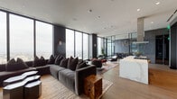 Located in the heart of Oakland at 1314 Franklin St, this sophisticated high-rise space offers a seamless blend of modern design and elevated functionality. Floor-to-ceiling glass windows dominate the perimeter, flooding the interior with natural light and framing breathtaking panoramic views of the Oakland skyline and beyond.

The expansive open-plan lounge area is anchored by a generously proportioned sectional sofa set atop a striped area rug, complemented by organic wood accent tables and sleek hexagonal coffee tables. Multiple seating arrangements create distinct yet connected zones, ideal for both relaxed gatherings and focused collaboration.

The gourmet kitchen is a standout feature, equipped with a substantial marble-topped island with built-in gas cooktop, a stainless steel range hood, and floor-to-ceiling custom cabinetry in a warm grey wood finish. A marble backsplash adds an elegant touch, while a secondary prep area with under-cabinet lighting and a stainless sink provides added utility.

A dedicated conference room commands attention with its deep navy geometric wallcovering, bold gold pendant lighting, and a richly stained wooden conference table — an impressive setting for professional meetings. Throughout, wide-plank hardwood flooring, recessed lighting, and dark accent walls contribute to a cohesive, upscale aesthetic.