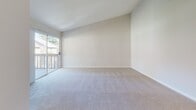 Located at 1420 S Highland Ave in Fullerton, California, this single-floor residence offers a clean, neutral aesthetic with a practical and open layout. The spacious living area is finished with plush carpeting and features generous wall space bathed in natural light. A ceiling fan overhead adds comfort, while a sliding glass door opens to a private balcony, bringing in outdoor views and additional brightness. The open pass-through connects the living area seamlessly to the kitchen, which is outfitted with white cabinetry, light countertops, and white appliances including an electric range with an over-the-range microwave. The kitchen flooring transitions to warm tile, adding a subtle contrast to the carpeted living spaces. A hallway leads to additional rooms, including a well-appointed bathroom featuring tile flooring, a single vanity with white cabinetry, a large mirror, and a shower/tub combination. Throughout the residence, the consistent use of white walls, light tones, and clean finishes creates a bright and airy atmosphere. The layout is efficient and functional, making excellent use of the available space on a single level.